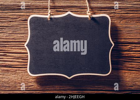 Empty black chalkboard sign hanging on rope on wood background Stock Photo