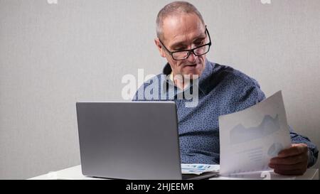 Senior man sits near computer checking reports in office Stock Photo