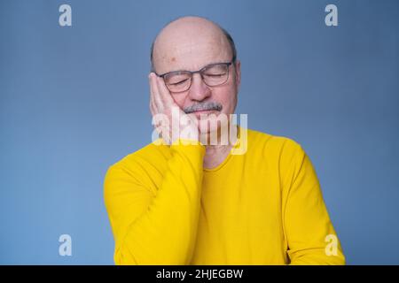 Senior man in glasses sleeping tired dreaming smiling with closed eyes. Studio shot Stock Photo