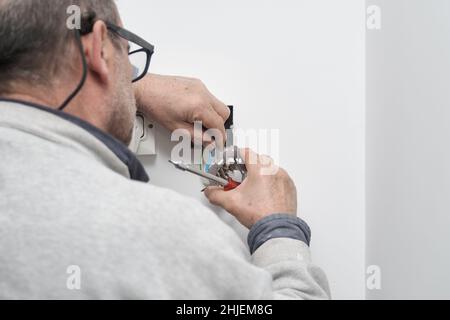 Senior electrician connecting power wires to the plug on a house. Stock Photo