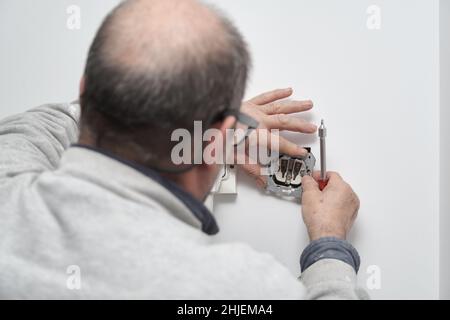 Senior electrician installing new current socket with screwdriver. Stock Photo