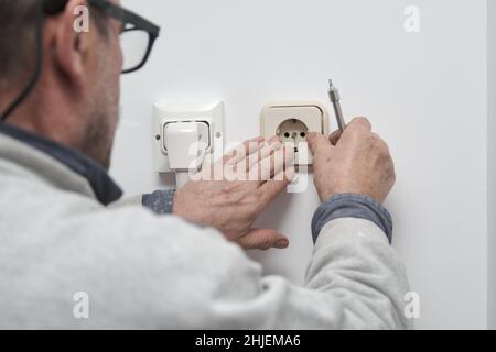 Senior electrician installing an electrical plug in a new house. Stock Photo