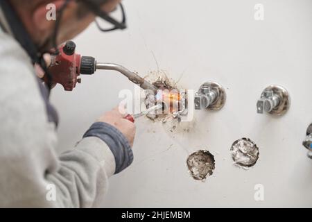 Professional senior plumber soldering copper pipes with a gas burner. Stock Photo