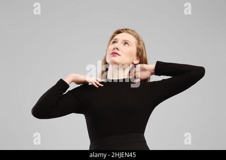 Low angle photo of young woman lifting hands to her shoulders and looking up in studio over grey background Stock Photo