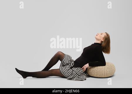 Full length studio portrait of young wooman sitting on the floor in profile over grey background Stock Photo