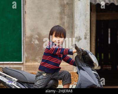 Little Vietnamese girl sitting on a motorcycle and looking at the camera Stock Photo