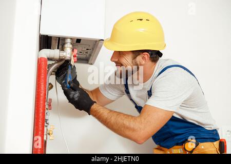 Side view of handyman, technician using screwdriver while fixing boiler or water heater, working on heating system in apartment Stock Photo