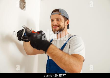 Hard working electrician, handyman using pliers for cutting wires, working on electric system in new apartment Stock Photo