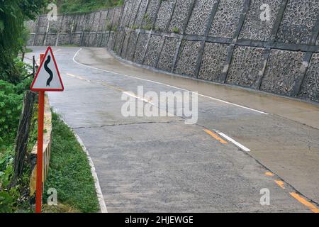 Road sign in the edge of wet winding road. An early warning sign for drivers before the curve. Stock Photo