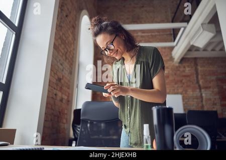 Smiling woman, interior designer or architect taking photo of a blueprint using smartphone, working on new project, standing in her office Stock Photo