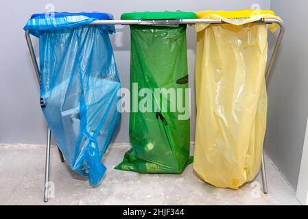 Three garbage bags for segregating glass, foil and paper standing on a rack in the garage with the lid closed. Stock Photo