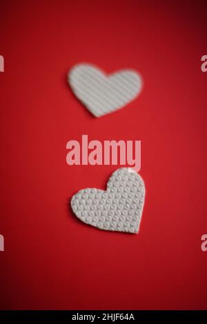 Two white fabric hearts on vivid red table. Stock Photo