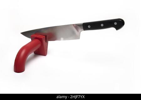 Close up of high quality large sharp meat kitchen knife being pulled over red plastic knife sharpener on white background concept for knife sharpening Stock Photo
