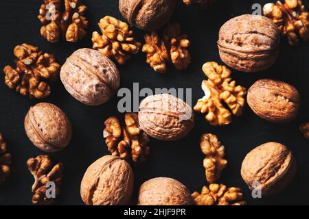 Whole and peeled walnuts on a black background. Close-up, flat lay, top view. Food background, selective focus. Stock Photo