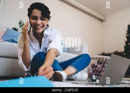 Positive young woman talking on smartphone during work online Stock Photo