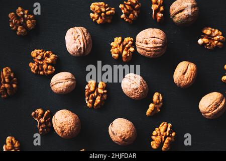Whole and peeled walnuts on a black background. Close-up, flat lay, top view. Food background, selective focus. Stock Photo