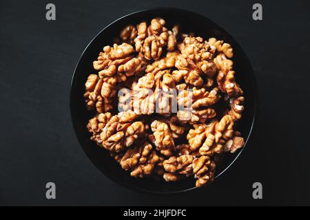 Peeled walnuts in a black bowl on a black background. Close-up, flat lay, top view. Food background, selective focus. Stock Photo