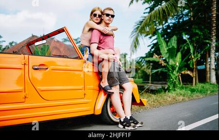 Couple sitting on retro car and hugging Stock Photo