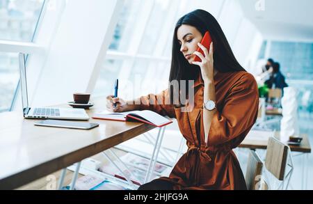 Young woman making notes and talking on phone Stock Photo