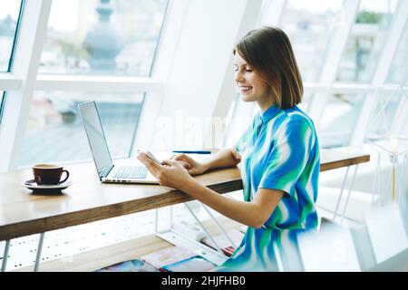 Smiling female freelancer browsing smartphone in light workplace Stock Photo