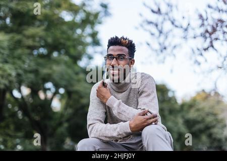 Smiling African American man in turtleneck vest talking on his phone in a park Stock Photo