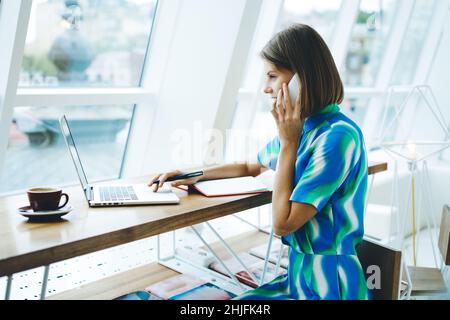 Smiling female student talking on smartphone in modern workplace Stock Photo
