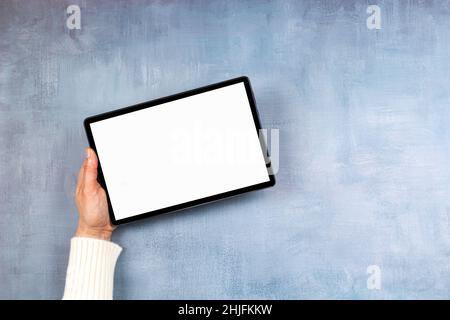 Woman hand holding digital tablet computer with blank white screen mock up on gray color background. Top view, copy space Stock Photo