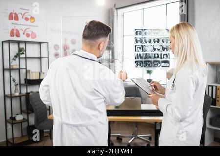 Medical experts in white lab coats writing on flipchart while analysing results of x ray scan. Man and woman having meeting at hospital about severe patient diagnosis. Stock Photo