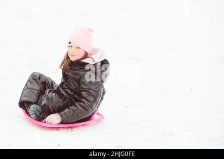 Active girl sliding down the hill. Happy child having fun outdoors in winter on sledge. Family time. Stock Photo