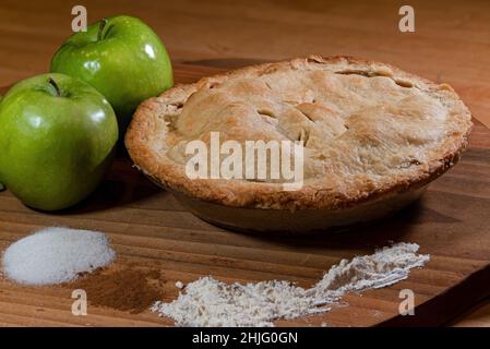 Fresh baked double crust apple pie displayed with key ingredients of green tart apples, sugar, cinnamon, and flour. Stock Photo