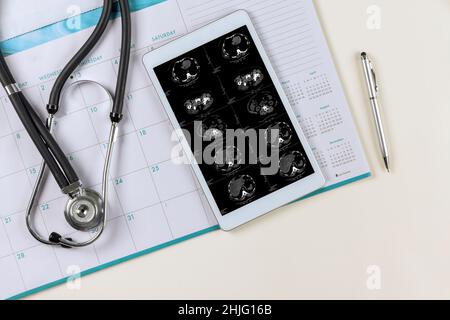 MRI scan of a human head showing in digital tablet result for patient with medical documents on desk of doctor workplace the planning survey Stock Photo