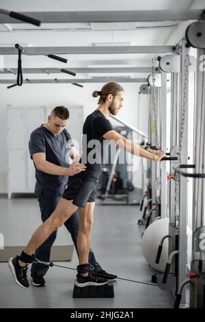 Man doing exercises on decompression simulators with the help of rehabilitation specialist Stock Photo