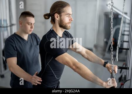 Man doing exercises on decompression simulators with the help of rehabilitation specialist Stock Photo