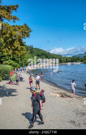 People on beach at Luss beside Loch Lomond. With Lodge on Loch Lomond hotel in background. Stock Photo