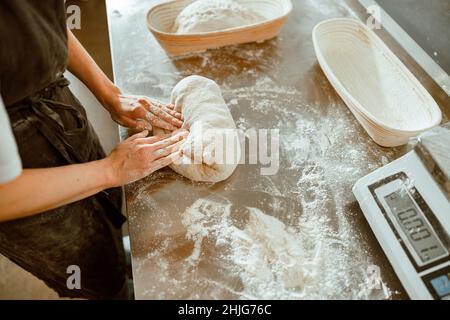 aker in apron kneads raw dough made of wheat flour in contemporary shop Stock Photo