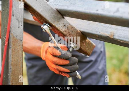 Close up of man hand in work glove tightening bolt with stainless steel wrench. Male worker using wrench tool while installing metal rails for solar panel system. Stock Photo