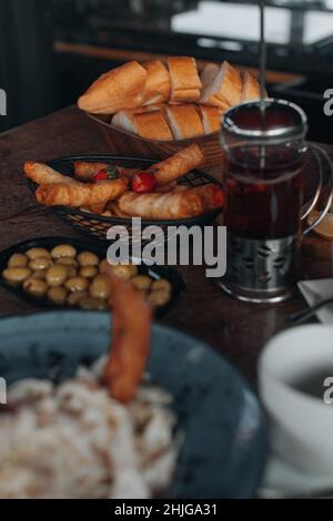 Fresh pastries, green olives, white bread and black tea in a teapot on the table. Traditional Turkish food Stock Photo