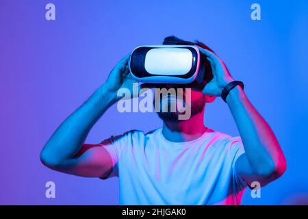 Metaverse concept. European young man in vr glasses, playing video games with virtual reality headset, trying to touch something with hand. Stock Photo