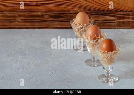 three chicken eggs in crystal glasses, decorated with hay imitation, Easter concept, copy space, selective focus, idea of Easter table decorartion Stock Photo