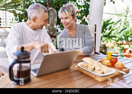 Senior caucasian couple smiling happy having breakfast and using laptop at the terrace. Stock Photo