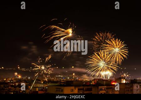 A lot of bright fireworks in the night sky over a city. Townspeople launching fireworks during New Year celebrating at midnight. Outdoor night scene. Stock Photo