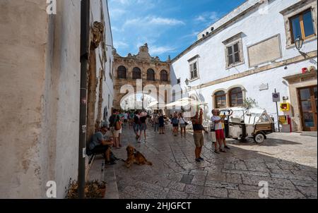 Ostuni, Puglia, Italy. August 2021. In the heart of the historic center of the village a large arch connects two houses. Beautiful summer day, people Stock Photo