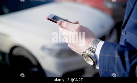 Close-up of businessman pressing car key. Action. Businessman opens car with electronic key and looks at phone. Modern car key to open and start it. Stock Photo