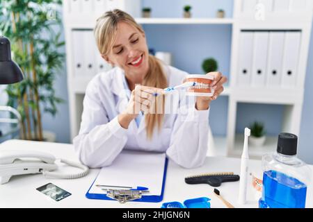 Young blonde woman wearing dentist uniform using teethbrush at clinic Stock Photo