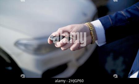 Close-up of businessman pressing car key. Action. Businessman opens car with electronic key and looks at phone. Modern car key to open and start it. Stock Photo