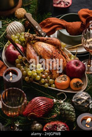 Christmas or New Year holiday dinner festive table setting with chicken, fruit, poached pears, hot spiced wine. Black linen tablecloth with dishes, ca Stock Photo