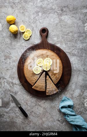 A sliced lemon cake on a wood cutting board with fresh lemons Stock Photo