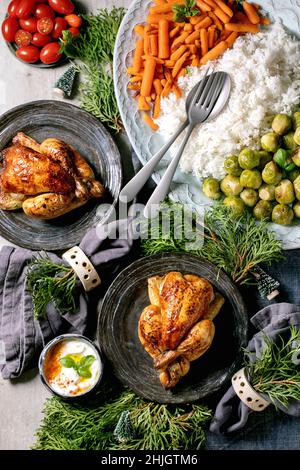 Christmas festive dinner table with grilled chicken, rice and vegetables baked brussel sprouts, baby carrot in ceramic bowls, xmas decorations on blue Stock Photo