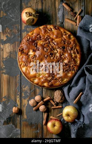 Sweet homemade apple and walnuts cake Charlotte on plate with fresh gardening apples, cinnamons and nuts around over dark wooden plank background. Aut Stock Photo