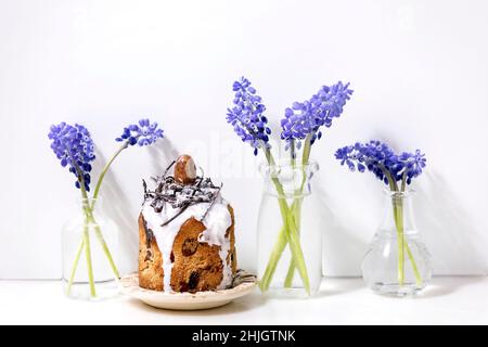Homemade traditionla Easter kulich cake with chocolate nests and eggs on ceramic plates decorated with muscari flowers on white marble table. Traditio Stock Photo